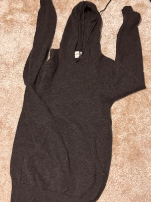  John Henric kasmhir  - Mjuk och lyxig mörkgrå hoodie från John Henric i 100% kashmir. Tröjan har huva med snörning, ribbade muddar och lång ärm. Perfekt för dig som vill ha en chill och stilren look med extra komfort. Hör av er vi mer frågor