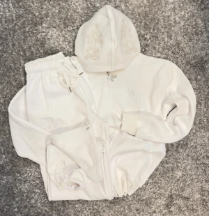 Decrese Sweden 🇸🇪 Set – Vit med silverdetaljer (S) - Decrese Set – Vit med silverdetaljer (S) Unisex hoodie + byxor i mjuk bomull med lätt stretch och stentvättad finish. Vit broderad logga samt ljusa silveraktiga detaljer på rygg och huva. Byxor: midja 30–42 cm, innerben 68 cm, ytterben 94 cm, 2 fram- och 2 bakfickor, resår+dragsko. Hoodie: axel 50 cm, bröst 50 cm, längd 64 cm, ärm 60 cm, 2 fickor. Storlekar XS–M. Skickas inom 1–2 dagar. Köparen står för returfrakt.