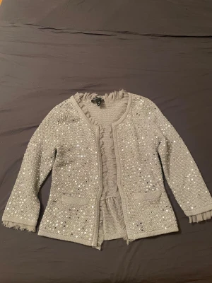 Jul/Nyår cardigan💕 - Säljer en glittrig silverfärgad cardigan jacka från Spirit med paljetter över hela ytan. Jackan har långärmade ärmar, två fickor fram och snygga volangdetaljer vid kanterna. Perfekt för dig som vill sticka ut och addera extra bling till din outfit.