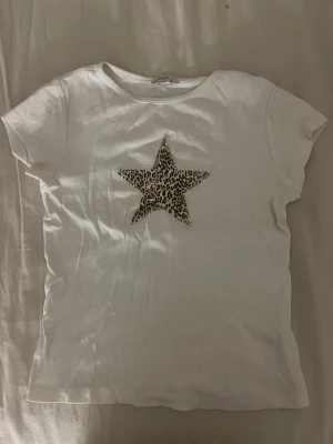 Vit t-shirt med leopardstjärna Subdued - Vit t-shirt från Subdued i storlek S med en stjärna i leopardmönster på bröstet. T-shirten har rund hals och korta ärmar. (Har en liten smink fläck vid halsen) men tvättas innan jag fraktar. 