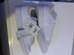 Adidas Stan Smith W vita sneakers - Fräscha Adidas Stan Smith W sneakers i helvitt med beige detaljer och snygg broderad häl, klassiskt låga. Helt oanvända med prasselskiten kvar i skon, tyvärr utan orginal skokartongen. 