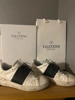 Valentino Garavani Open sneakers vit/svart - Säljer ett par Valentino Garavani Open sneakers i vit kalvskinn med bred svart läderpanel över mitten. Klassisk rund tå, platt sula och vita snören. Snygg och stilren design med logga på sulan. Box och dustbag medföljer.