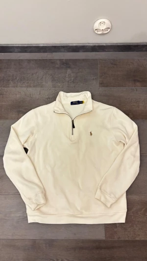 Ralph Lauren quarter zip - Snygg beige långärmad tröja från Polo Ralph Lauren med klassisk broderad logga på bröstet. Tröjan har en half zip-dragkedja och hög krage, tillverkad i mjuk bomull. Perfekt för dig som gillar stilrena och tidlösa plagg.