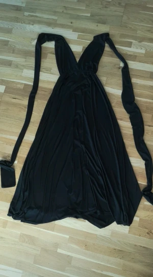 Svart infinityklänning - Svart infinityklänning i mjukt och följsamt material. Klänningen är lång och har långa band som kan stylas på över 100 olika sätt, t.ex. omlott, axelbandslös, one shoulder eller med knyt. Perfekt för dig som vill ha en klänning med många möjligheter och personlig stil.