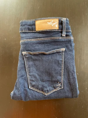 Mörkblå skinny jeans - Snygga mörkblå jeans med klassisk femficksdesign och kontrastsömmar. Modellen är skinny med låg midja och tillverkad i stretchigt jeansmaterial för en schysst passform. Perfekt för dig som gillar en smal siluett och stilren look.