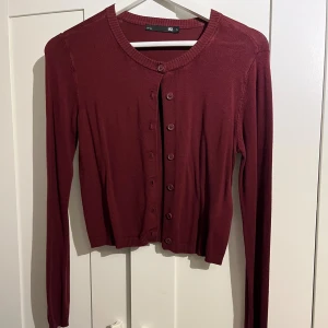 Vinröd kofta med knappar - Snygg vinröd kofta från H&M med rund halsringning och långa ärmar. Koftan har ribbade muddar och knäppning framtill med matchande knappar. Perfekt att slänga över en topp för en chill look.