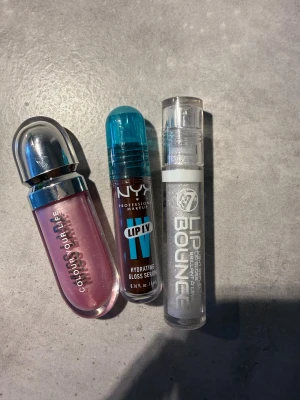 3 läppglans från NYX, W7 & Colour Your Life - Säljer tre läppglans: ett rosa med metalliclock från Colour Your Life, ett NYX Lip IV Hydrating Gloss Serum med blått lock och ett W7 Lip Bounce med transparent hylsa och glittereffekt. Perfekt för dig som vill ha glossiga och återfuktade läppar.