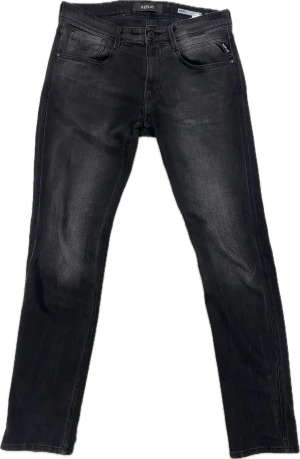 Replay Anbass svarta jeans - Svarta Replay Anbass jeans med snygg tvättad look och klassiska fem fickor. Slimmad passform och raka ben, med diskreta Replay-loggor på fickorna. Jeansen är tillverkade i stretchigt denim för extra komfort och stil.