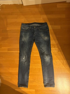 Blå skinny jeans från Dondup - Snygga blå jeans från Dondup med slitna detaljer och skinny passform. Klassisk femficksmodell med orange sömmar och diskret logga bak i midjan. Jeansen är tillverkade i denim och har en modern, smal siluett som sitter tajt hela vägen ner.