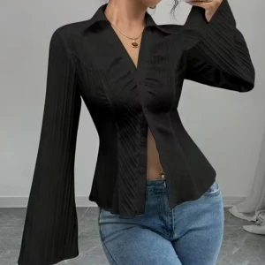 Svart figursydd skjorta med vida ärmar - Snygg svart skjorta med figurnära passform och vida, långärmade ärmar. Skjortan har v-ringad krage, knappar framtill och subtila veckade detaljer som ger en cool look. Perfekt att styla med jeans eller kjol för en trendig outfit.