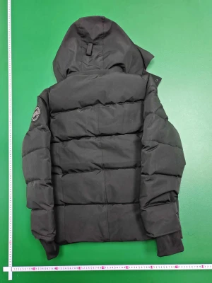 Svart pufferjacka från Canada Goose - Svart pufferjacka från Canada Goose med stor huva och snygg pälsdetalj. Jackan har quiltad design, dragkedja och knappar framtill samt ribbade muddar vid ärmslut. Märkespatch på ärmen och insidan. Perfekt för kalla dagar och riktigt stilren look.