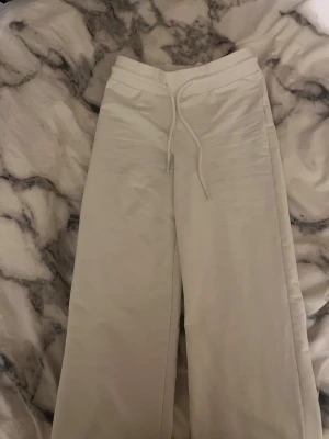 Vita wide mjukisbyxor med snörning - Säljer ett par vita mjukisbyxor med breda ben och snörning i midjan. Byxorna har en relaxed passform och är tillverkade i mjukt bomullsmaterial. Perfekta för chill dagar och har en enkel, clean look.