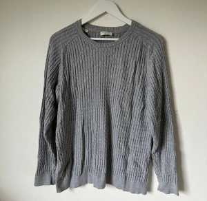 Grå kabelstickad tröja från Selected Homme - Snygg grå tröja från Selected Homme i storlek L. Tröjan är kabelstickad med rund hals och långa ärmar, tillverkad i 100% ekologisk bomull. Perfekt för dig som gillar stilrena och bekväma plagg med lite struktur. 4Ö16