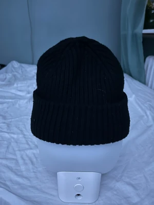 Svart ribbad mössa från Parajumpers - Svart ribbstickad mössa från Parajumpers med uppvikt kant och snyggt broderat PJS-märke framtill. Klassisk form som sitter skönt på huvudet och passar perfekt när det är kallt ute. Materialet är mjukt och värmande.