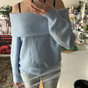 Ljusblå offshoulder stickad tröja - Superfin ljusblå stickad tröja med bred ribbad offshoulder-krage. Tröjan har lång ärm och en loose fit som ger en chill vibe. Perfekt att styla med jeans för en avslappnad look.