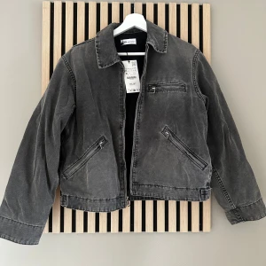 Grå jeansjacka från Zara XS - Säljer en grå jeansjacka från Zara i storlek XS. Jackan har klassisk krage, raka ärmar och tre dragkedjeförsedda fickor framtill. Materialet är robust denim och modellen är något croppad med snygga sömdetaljer. 💕Sprillans ny endast testad med lappar kvar. 