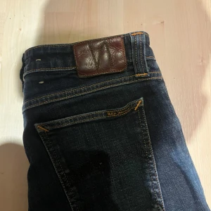 Mörkblå  jeans från Nudie Jeans - Snygga mörkblå jeans från Nudie Jeans i klassisk femficksmodell. Jeansen har skinny passform, orangea kontrastsömmar och är tillverkade i slitstarkt denim. Perfekta för dig som gillar en smal siluett och stilren look.