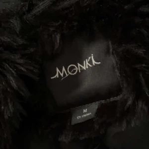 Svart pälsjacka från Monki - Säljer en svart pälsjacka från Monki i storlek M. Jackan är fluffig och har en klassisk rak passform med långa ärmar. Perfekt för dig som vill ha en mysig och snygg look under kyliga dagar.