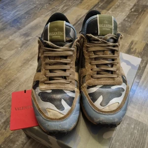 Valentino Garavani Rockrunner sneakers - Säljer ett par Valentino Garavani Rockrunner nypris‼️ 6100kr ‼️sneakers med camouflagemönster i grönt, beige, blått och svart. Skorna har bruna mockadetaljer, snörning och coola röda detaljer med nitar på hälen. Kombination av skinn, mocka och textil för en unik streetstil.