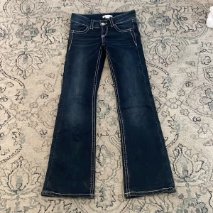 Mörkblå bootcut jeans Gina Tricot 140 - Mörkblå jeans från Gina Tricot i storlek 140 med kontrasterande vita sömmar och snygga broderade detaljer på bakfickorna. Bootcut-modell med jätte låg midja❣️Bara använda några få ggr