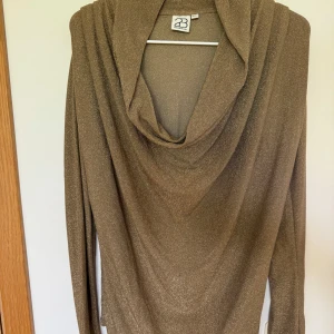 Guldig Glittrig långärmad topp från 2B - Snygg guld glittrig topp från 2B med lång ärm och draperad, djup urringning. Materialet är mjukt och stretchigt, perfekt för dig som vill sticka ut med lite extra shimmer. Passar dig som gillar en elegant och trendig look. Storlek S/M 