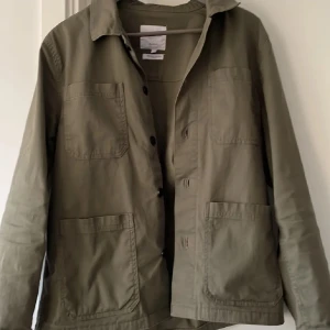 Grön overshirt från Lindbergh - Stilren ogrön overshirt från Lindbergh med relaxed fit. Jackan har fyra stora fickor framtill, klassisk krage och knäppning med svarta knappar.