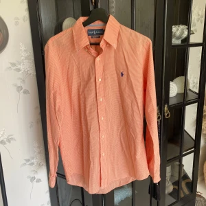 Rutig orange skjorta från Ralph Lauren - Orange och vit rutig skjorta från Ralph Lauren i custom fit-modell. Skjortan har klassisk krage, långa ärmar och knäppning framtill. Storlek M 