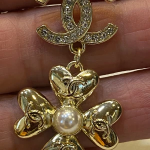  örhängen med pärldetalj - Supersnygga örhängen i guld med hängande blommor med hjärtformade blad. Varje blomma har en pärlliknande detalj i mitten och små logar på varje blad. Perfekta för dig som vill sticka ut med lyxig vibe.