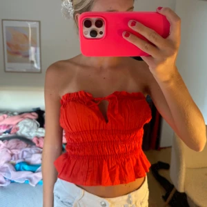 Röd bandeau tubtopp med volang - Säljer en röd bandeau tubtopp med smockad midja, volangkant nertill och söt knytning framtill. Från hm i storlek XS 