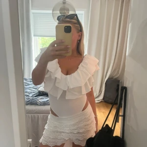 Vit volangblus med djup urringning - Supersöt vit blus med stora volanger runt urringningen och axlarna. Modellen är ärmlös och har en figurnära passform som framhäver midjan. Perfekt för dig som gillar romantiska och trendiga plagg. Materialet känns mjukt och lätt. (Första bilden är tagen av en annan användare som jag köpte den utav) 