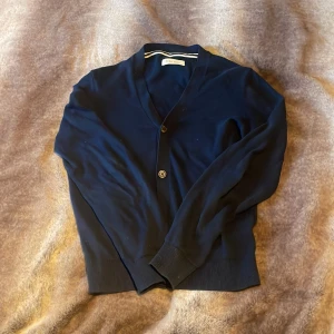 Mörkblå kofta från Pier One - Snygg mörkblå kofta från Pier One med klassisk v-ringning och knäppning framtill. Tröjan har långa ärmar, ribbade muddar och är tillverkad i mjuk bomull. Perfekt för lager-på-lager och enkel att matcha med olika outfits.
