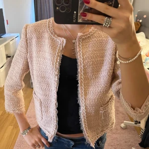 Ljusrosa kavaj från Hallhuber Donna - Superfin ljusrosa kavaj i bouclé från Hallhuber Donna. Jackan har rundad hals, trekvartsärm och råa kanter. Två fickor framtill och snygg struktur i tyget ger en chic vibe. Perfekt att slänga över en topp för en trendig look💕