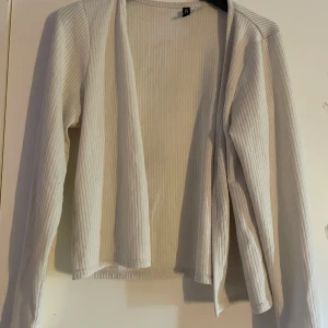 Ribbad vit kofta från H&M Divided - Ribbad, öppen vit kofta från H&M Divided i storlek L. Långärmad och i mjukt bomullsmaterial, perfekt att slänga över en topp eller klänning. Enkel och stilren design med raka linjer och utan knappar.