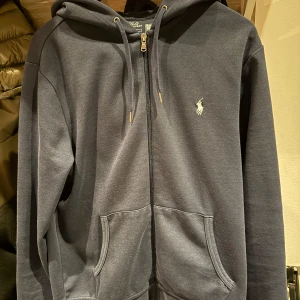 Ralph Lauren Zip-hoodie  - En mörkblå Ralph Lauren zip andväds väldigt få gånger säljer för att den inte passar längre, den är nopprig på vänster armbåge går att få bort har inte gjort det själv där med säljer jag billigare en vad jag tänkt 