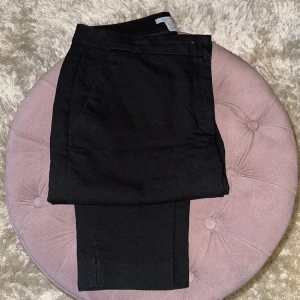 Svarta kostymbyxor från H&M, strl 36 - Svarta kostymbyxor från H&M i klassisk rak modell med diskreta fickor fram och en bakficka. Byxorna har en stilren look och är tillverkade i ett mjukt tyg som känns bekvämt hela dagen. Perfekta för en clean och snygg outfit.