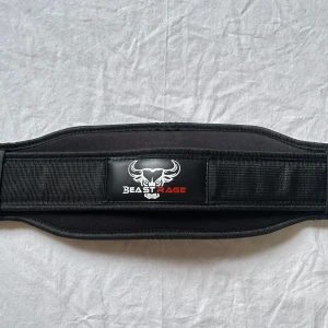 Svart träningsbälte Beast Rage M - Svart träningsbälte från Beast Rage i storlek M. Bältet är brett och vadderat för extra stöd vid tunga lyft och har en kraftig spänne. Perfekt för gymmet och styrketräning. Aldrig använt 