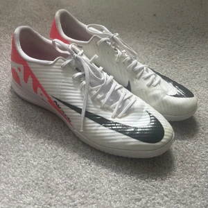 Nike Mercurial Zoom innefotbollsskor  - Säljer ett par Nike Mercurial Zoom fotbollsskor i vitt med svarta och neonröda detaljer. Skorna har snörning, platt sula och bra fäste.Perfekta för inomhusspel med sin greppvänliga yttersula och snygg design. Stl 45