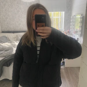 Svart quiltad pufferjacka från Zara - Quiltad svart pufferjacka från Zara i storlek S. Jackan har ett vågigt mönster i sömmarna, dragkedja framtill och två stora fickor. Materialet är mjukt och känns som bomull, med en loose passform och långärmade ärmar. Perfekt för kyliga dagar.