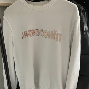 Vit sweatshirt från Jacob Cohën - Vit sweatshirt från Jacob Cohën med broderad logga i färgglada toner på bröstet. Tröjan har klassisk rund halsringning och är tillverkad i mjukt material som känns skönt mot huden. Perfekt för en avslappnad och stilren look.