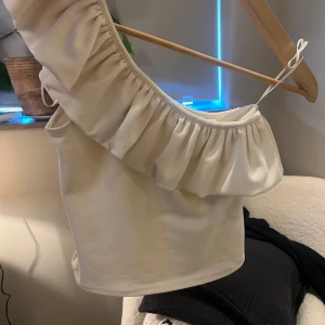 Vit offshoulder topp med volang H&M XS - Superfin vit offshoulder topp från H&M i storlek XS. Toppen har en bred volang längs halsringningen och är ärmlös med en axelbandslös design. Perfekt för dig som gillar en stilren och trendig look.