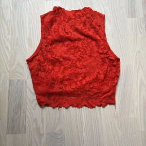 Röd spetsblus från FB Sister - Snygg röd blus från FB Sister i spets med fodrad insida. Ärmlös modell med en liten krage typ  och vågig kant nertill. Skick är jätte svårt att sätta då alla har olika åsikter om det, men för mig att det ett bra skick 