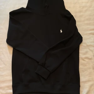 Svart hoodie från Ralph Lauren - Svart hoodie från Ralph Lauren med klassisk vit broderad logga på bröstet. Nytt skick