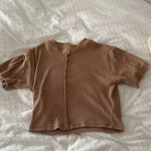 Beige croppad topp från Public Desire - Säljer en beige croppad topp från Public Desire i ribbat material. Toppen har korta ärmar, rund halsringning och en synlig söm framtill som ger en cool detalj. Perfekt att styla med matchande byxor eller jeans för en trendig look.
