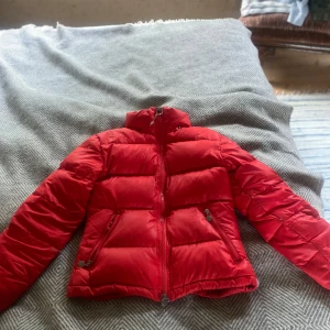 Röd Moncler pufferjacka med dragkedja -  Säljer min moncler köpt här på Plick! Har små hål lite här och där och därför ett billigt pris, den ska vara äkta! Den har inte Q:r koden då de är en äldre modell, säljer då jag ska köpa en ny! 💕