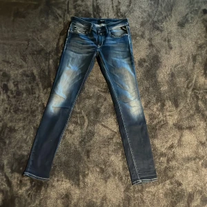 Replay blå skinny jeans med slitningar - Snygga blå jeans från Replay med skinny fit och coola slitningar. Klassisk femficksmodell med ljusa tvättade partier och kontrastsömmar. Bakfickorna har broderad detalj och läderpatch med Replay-logga i midjan. Perfekta för en trendig och avslappnad look.
