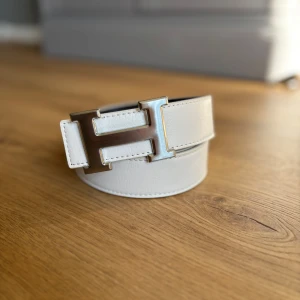 Vitt H-bälte - Riktig stilrent vitt bälte med ett silvrigt H. 110cm långt. Skick 10/10.