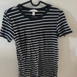 Vit randig marinblå t-shirt - Snygg marinblå t-shirt med vita horisontella ränder från H&M. Klassisk rund halsringning och korta ärmar. Perfekt för en avslappnad och stilren look. Tillverkad i mjuk bomull för skön komfort. I storlek XS och är aldrig använd.🤍