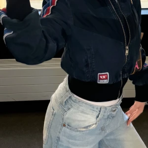 Mörkblå bomberjacka från Diesel -  Jag har köpt för 2600 men säljer den för 1400 för att ska inte använda längre.Säljer en mörkblå bomberjacka från Diesel med coola röda och vita detaljer på ärmarna. Jackan är croppad, har dragkedja framtill och en snygg logotyp på framsidan. Perfekt för dig som vill ha en sportig och trendig look.