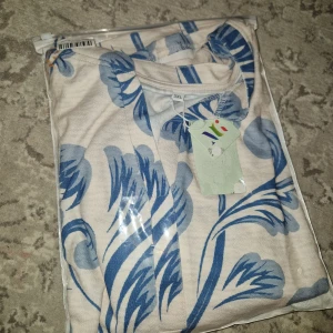 Blommig blus med volangärm 3XL - Ny snygg blus i vitt med stora blå blommor och coola volangärmar. Blusen har rund halsringning och trekvartsärm med extra volangdetalj. Perfekt för dig som gillar statementmönster och en luftig, bekväm passform.