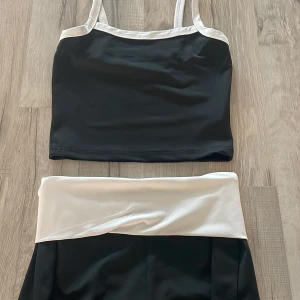 Svartvitt Pyamas set  - Säljer ett stilrent Pyamas set i svart och vitt. Toppen är bred med vita band och kanter, och shortsen har en bred vit linning upptill. Materialet är slätt och stretchigt, perfekt för mys sett Enkel men snygg design som sticker ut med sina kontrasterande färger.